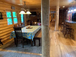Un interior de madera con una mesa de comedor, sillas, una zona de bar y piso de madera.