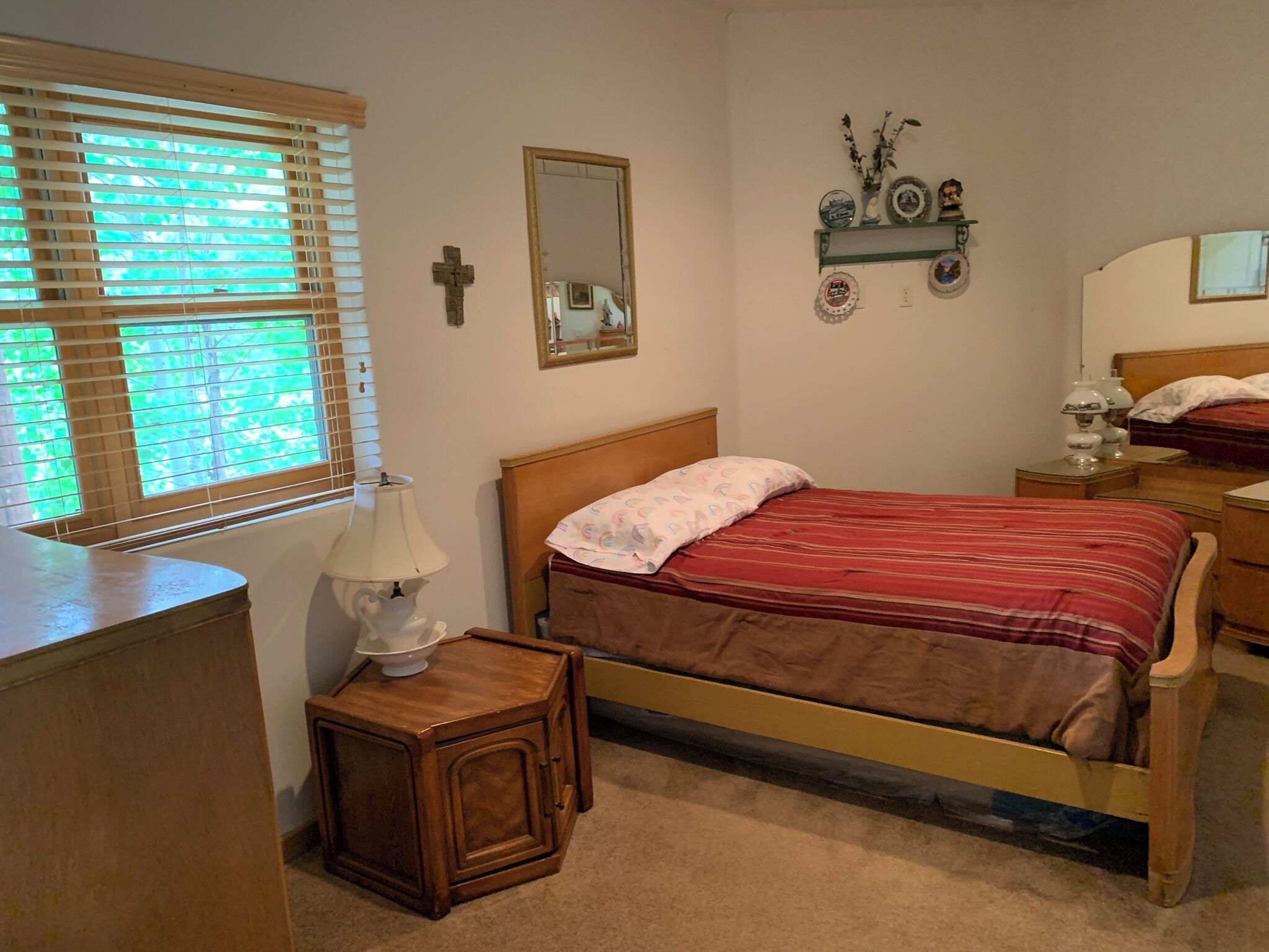 Un dormitorio con cama, mesitas de noche, una lámpara, un espejo y una ventana con persianas.