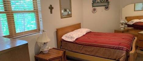 Un dormitorio con cama, mesitas de noche, una lámpara, un espejo y una ventana con persianas.