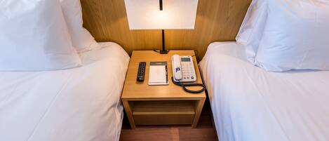 A hotel room with two beds, a bedside table with a lamp, a phone, and a notepad.