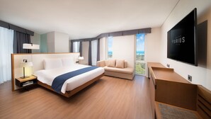 Una habitación de hotel moderna con una cama grande, un sofá, un televisor de pantalla plana y vistas al exterior.