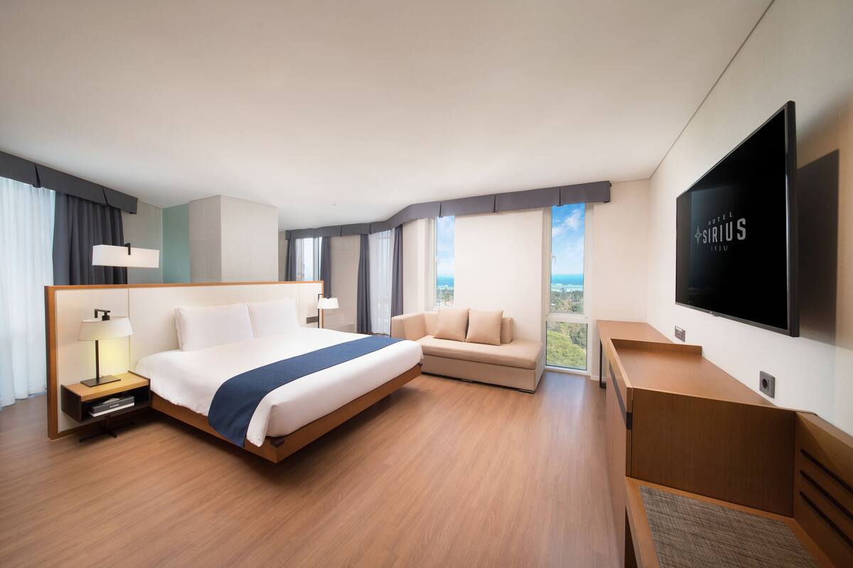 Una habitación de hotel moderna con una cama grande, un sofá, un televisor de pantalla plana y vistas al exterior.