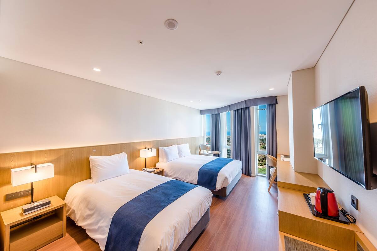 Habitación de hotel con dos camas, televisión, escritorio y ventana con cortinas.