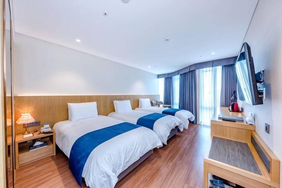 Una habitación de hotel con tres camas, un escritorio, un espejo y una mesita de noche.