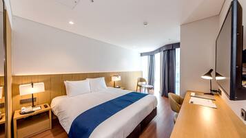 A hotel room with a large bed, bedside tables with lamps, a desk with a chair, and a large mirror.