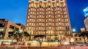 Un edificio moderno de gran altura con una fachada luminosa y una cuadrícula de ventanas, y un árbol en la parte delantera.