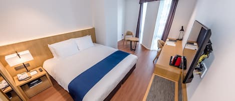 Een hotelkamer met een groot bed, een bureau met een computer, een stoel en een raam met gordijnen.