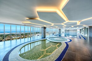 A modern indoor pool area with a view of the city and ocean.