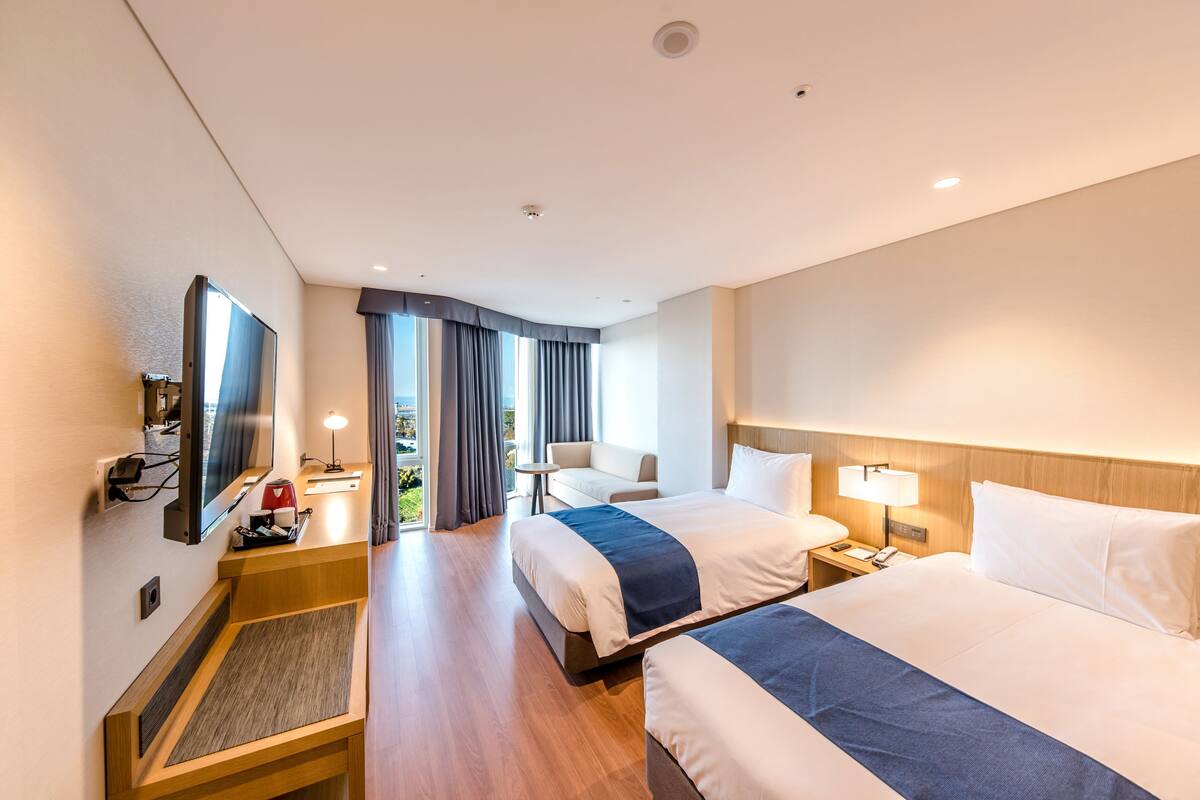 Una habitación de hotel con dos camas, un escritorio, un televisor y una ventana con cortinas.