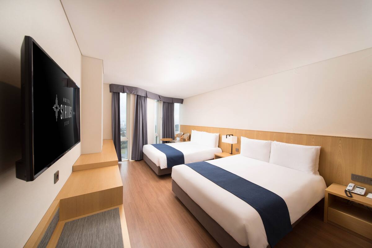 Habitación de hotel con dos camas, televisión y vistas a la ciudad.