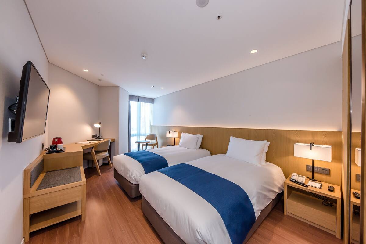 Una habitación de hotel moderna con dos camas, un escritorio, una silla y un televisor.