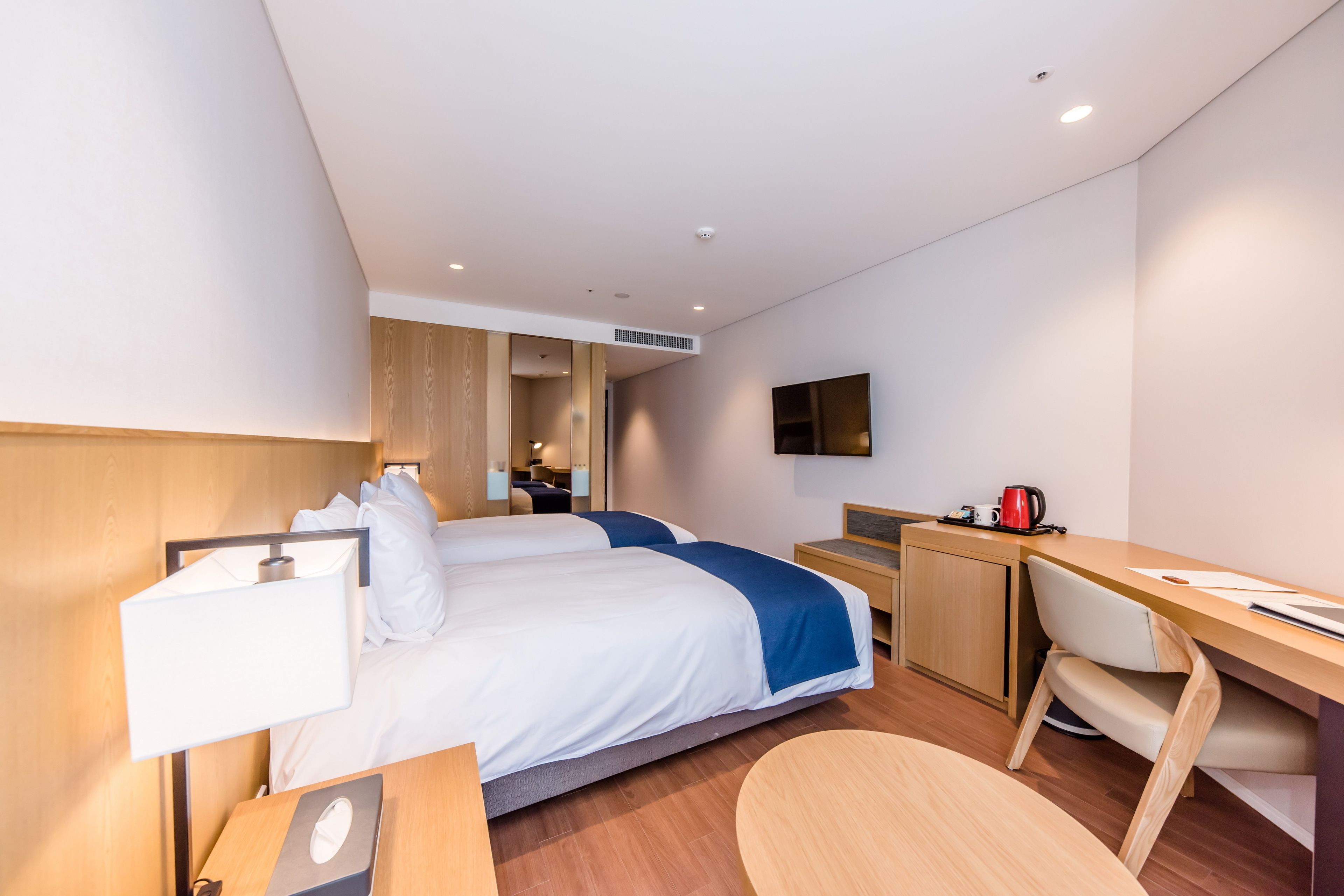 A modern hotel room with two beds, a desk, a chair, a TV, and a coffee maker.