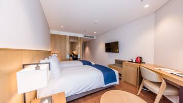 Una habitación de hotel moderna con dos camas, un escritorio, una silla, un televisor y una cafetera.