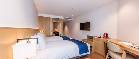 A modern hotel room with two beds, a desk, a chair, a TV, and a coffee maker.