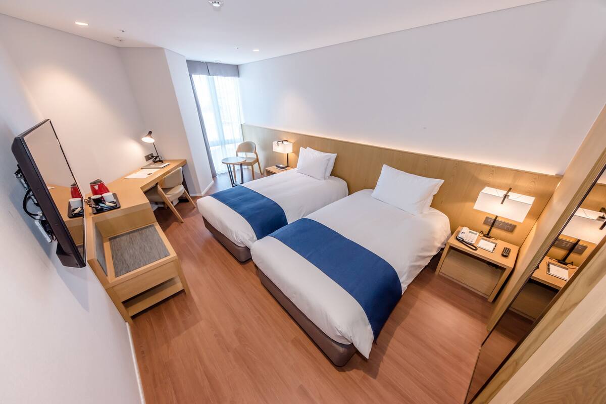 Una habitación de hotel con dos camas, un escritorio, una silla, un televisor y una ventana.