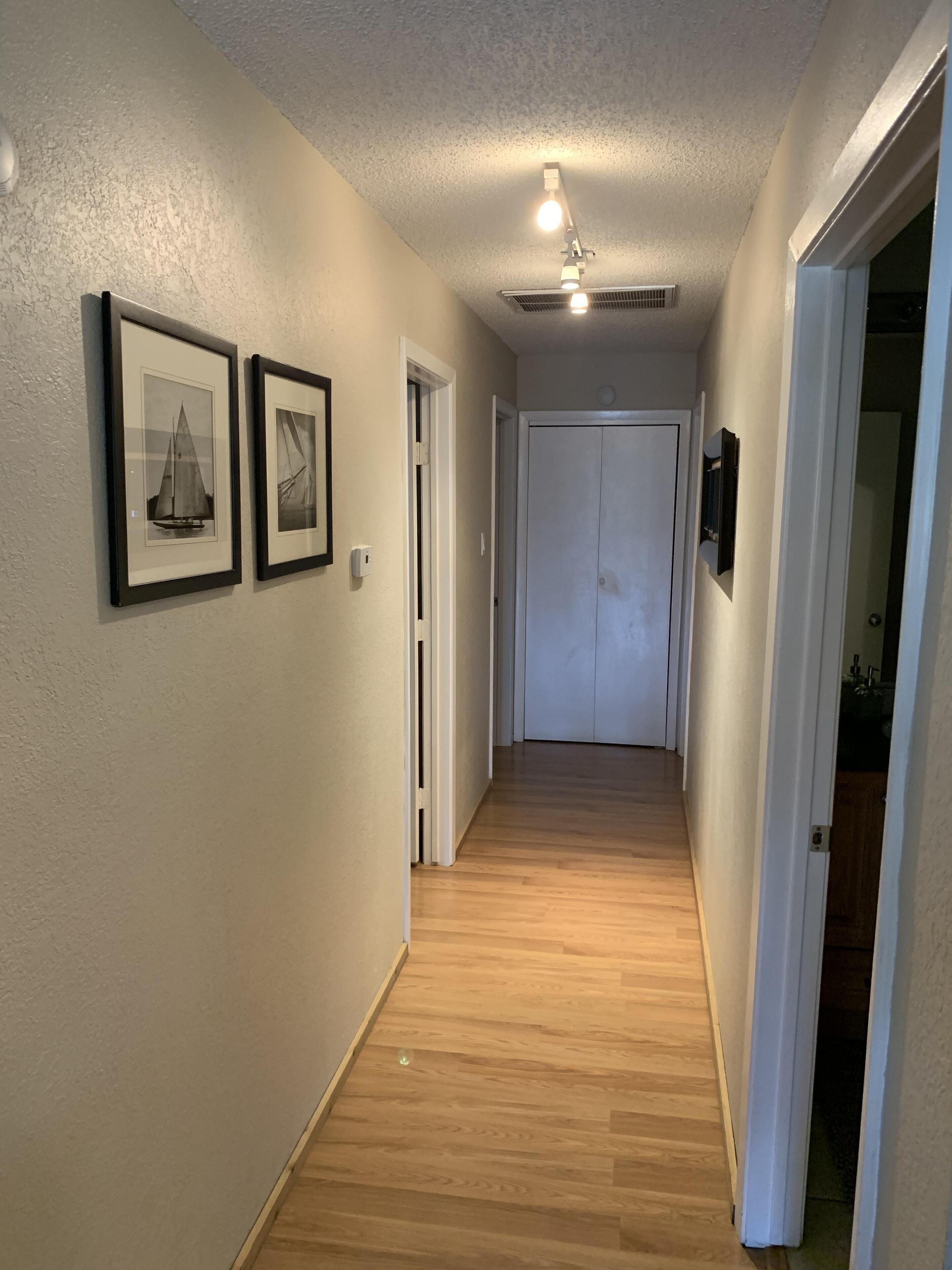 Un couloir doté d’un plancher en bois, de murs blancs et de deux tableaux encadrés. Une porte se trouve au bout du couloir.