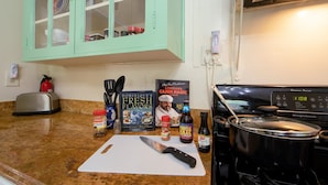 Una cocina con encimera de granito, tabla de cortar, cuchillo, libro de cocina, botella de salsa y estufa.