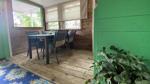 Un comedor con mesa y sillas de madera, ventanas amplias con persianas y una pared verde.