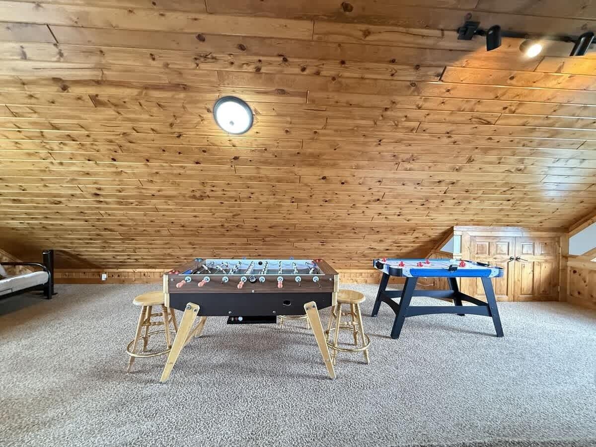 An attic room with two foosball tables, a wooden ceiling, and a carpeted floor.