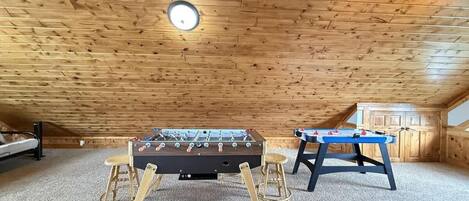 An attic room with two foosball tables, a wooden ceiling, and a carpeted floor.