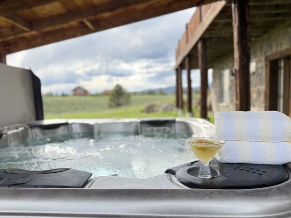 A hot tub with a glass of drink and a towel, set against a rural backdrop.