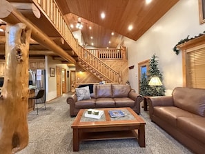 A spacious living area with a wooden staircase, leather sofas, and a coffee table.