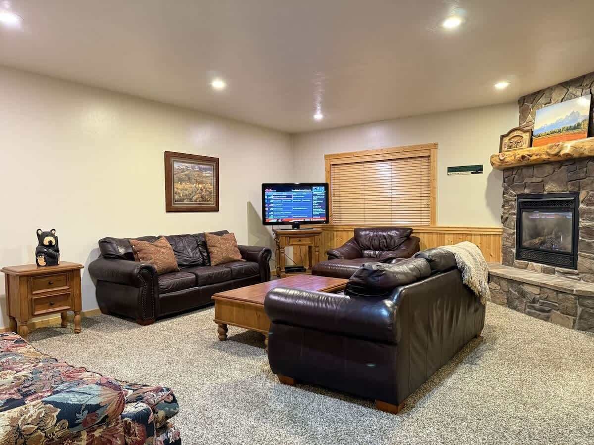 A cozy living room with leather sofas, a flat-screen TV, a fireplace, and a stone accent wall.
