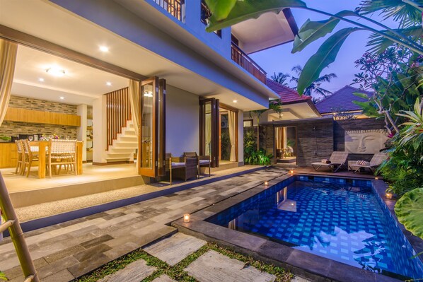 A modern house with a swimming pool, a dining area, and a staircase leading to a balcony. - LaMeli Villas Ubud (Ubud)