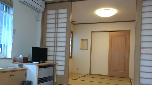 Una habitación japonesa tradicional con suelo de tatami, un televisor sobre una mesa baja y una puerta corredera.