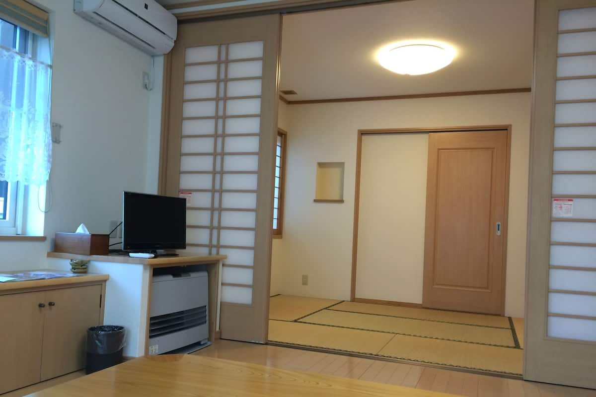 A traditional Japanese room with tatami flooring, a television on a low table, and a sliding door.