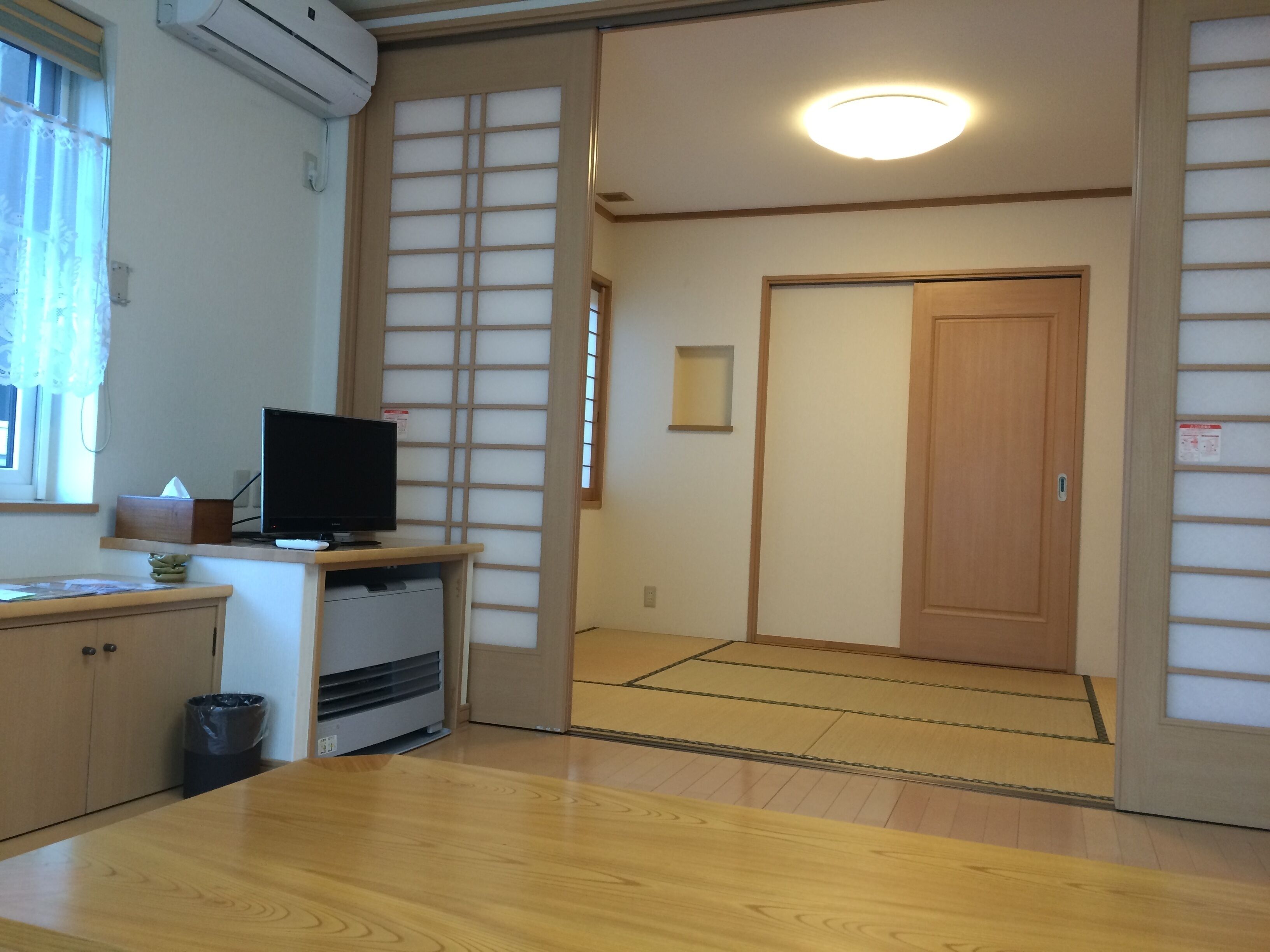 A traditional Japanese room with tatami flooring, a television on a low table, and a sliding door.