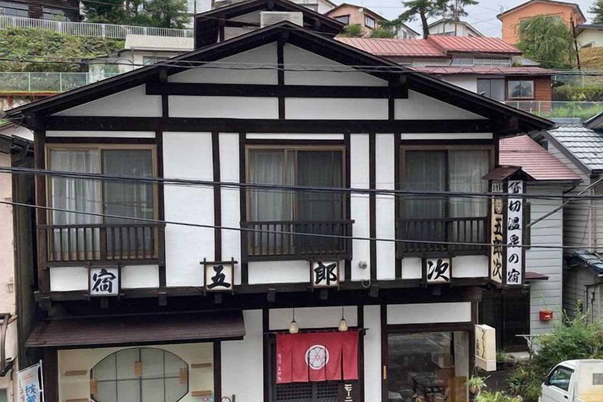 A traditional Japanese building with a two-story structure, a balcony, and a storefront with a red awning.