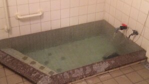 Un baño pequeño con azulejos, una bañera, un asidero blanco y un enchufe visible.