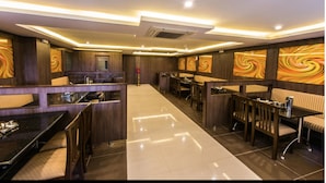 A modern restaurant with a long counter, booths, and a central dining area. - Plazza hotel , Trichy (Tiruchirappalli)