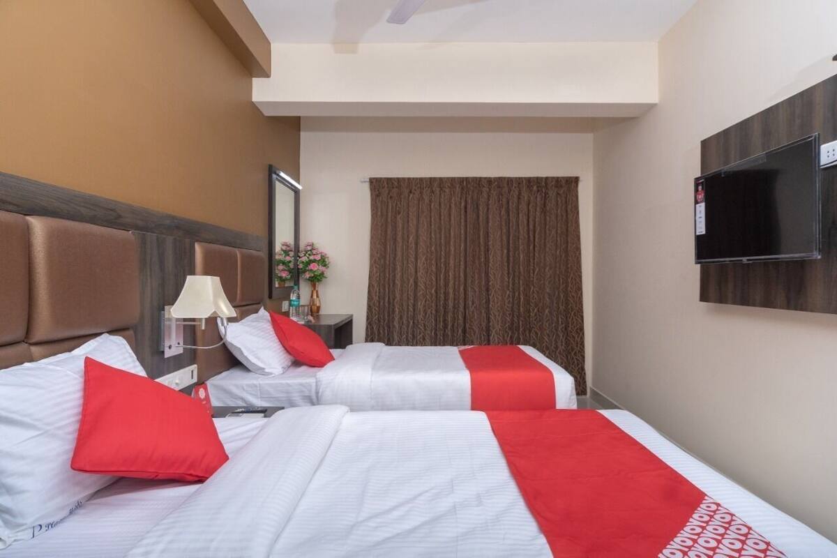 A hotel room with two beds, a TV, a lamp, and a curtain.