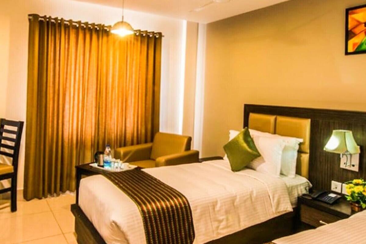 A hotel room with two beds, a desk, a chair, a lamp, and a painting on the wall.