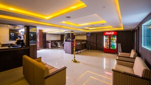 A lobby with a reception desk, seating area, and a Coca-Cola refrigerator. - Plazza hotel , Trichy (Tiruchirappalli)