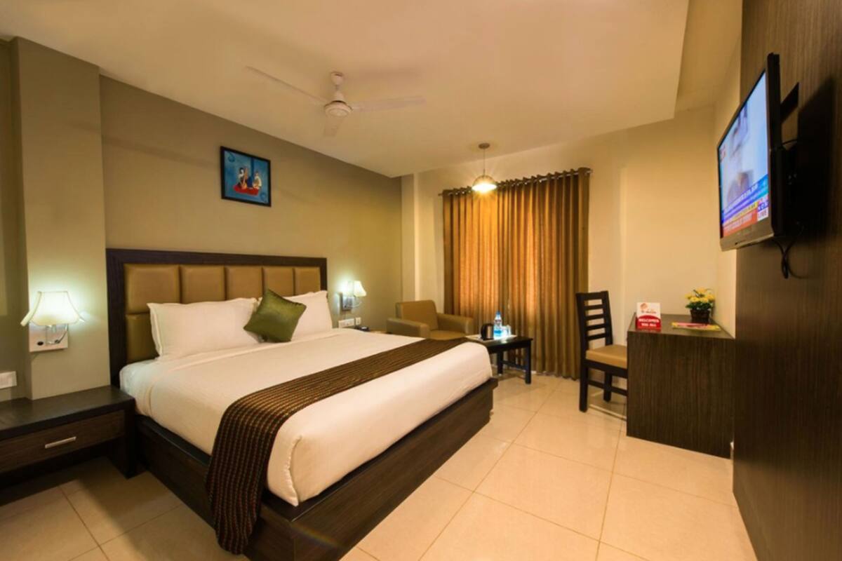 A hotel room with a large bed, a desk, a chair, a television, and a ceiling fan.