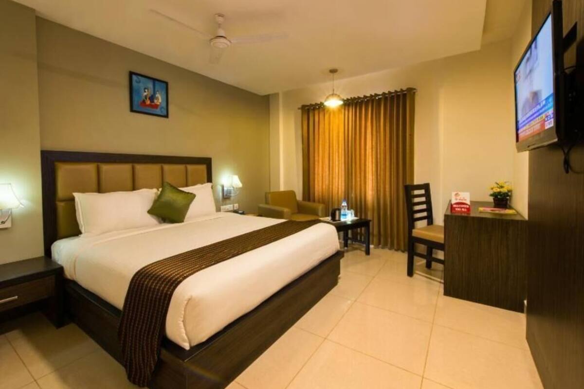 A hotel room with a bed, a desk, a chair, a television, and a ceiling fan.