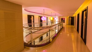 A hotel corridor with a glass railing, a curved staircase, and a ceiling with decorative lighting. - Plazza hotel , Trichy (Tiruchirappalli)