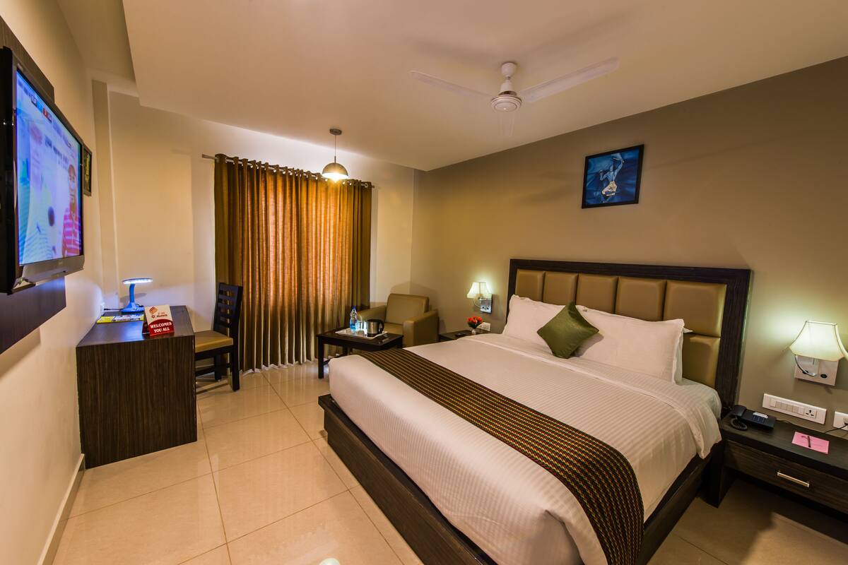 A hotel room with a bed, a desk, a chair, a nightstand, a TV, and a ceiling fan.