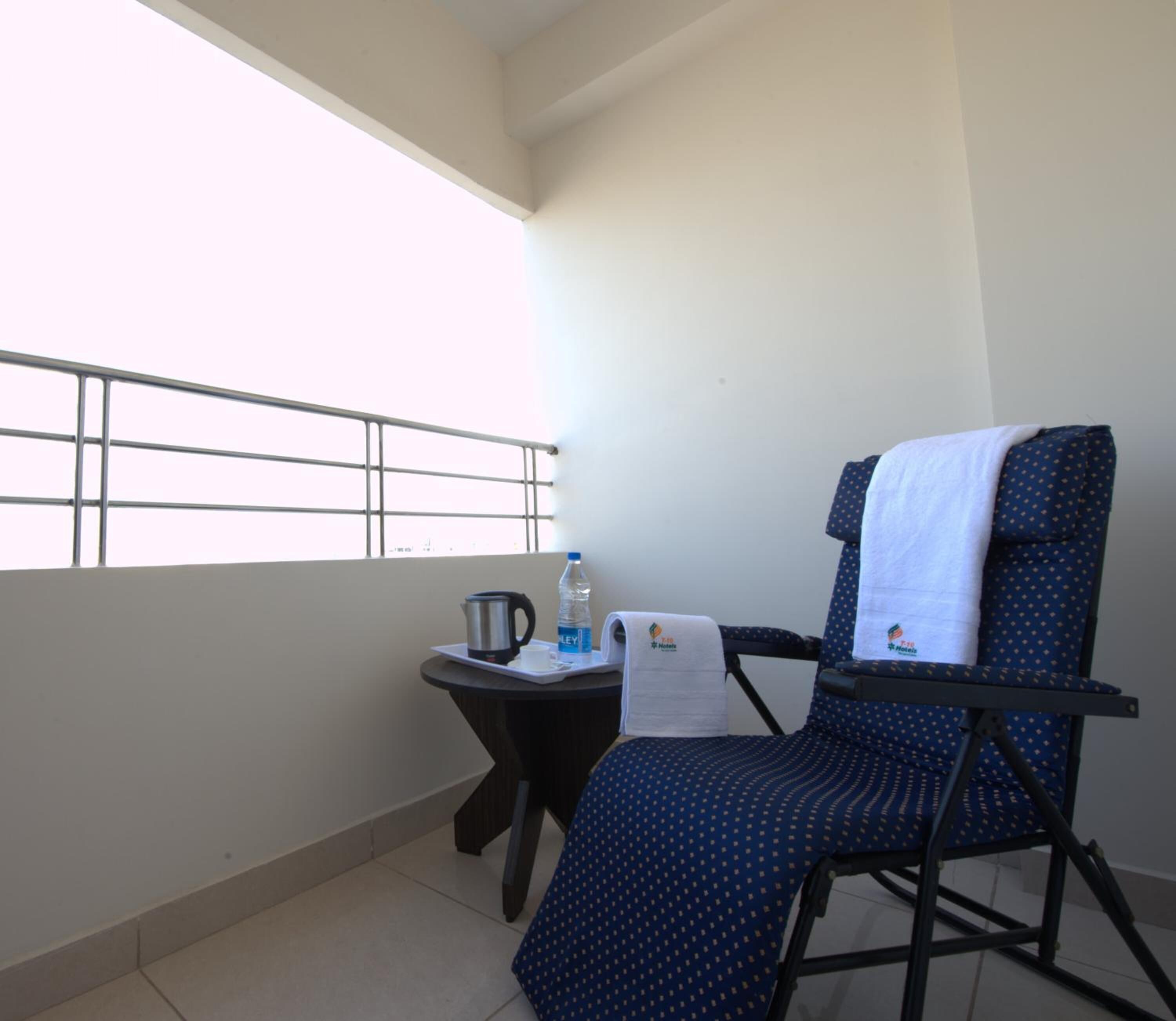 A balcony with a chair, a small table, a kettle, a bottle of water, and a towel.