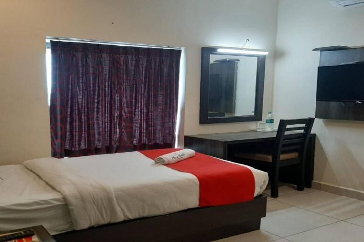 A hotel room with a bed, a desk, a chair, a TV, and a window with curtains.