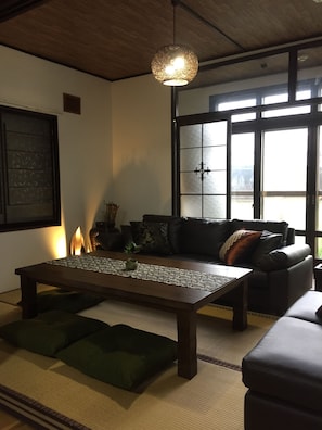 Ein modernes Wohnzimmer mit einem Holztisch, einer Couch und Kissen. Ein großes Fenster bietet einen Blick ins Freie.