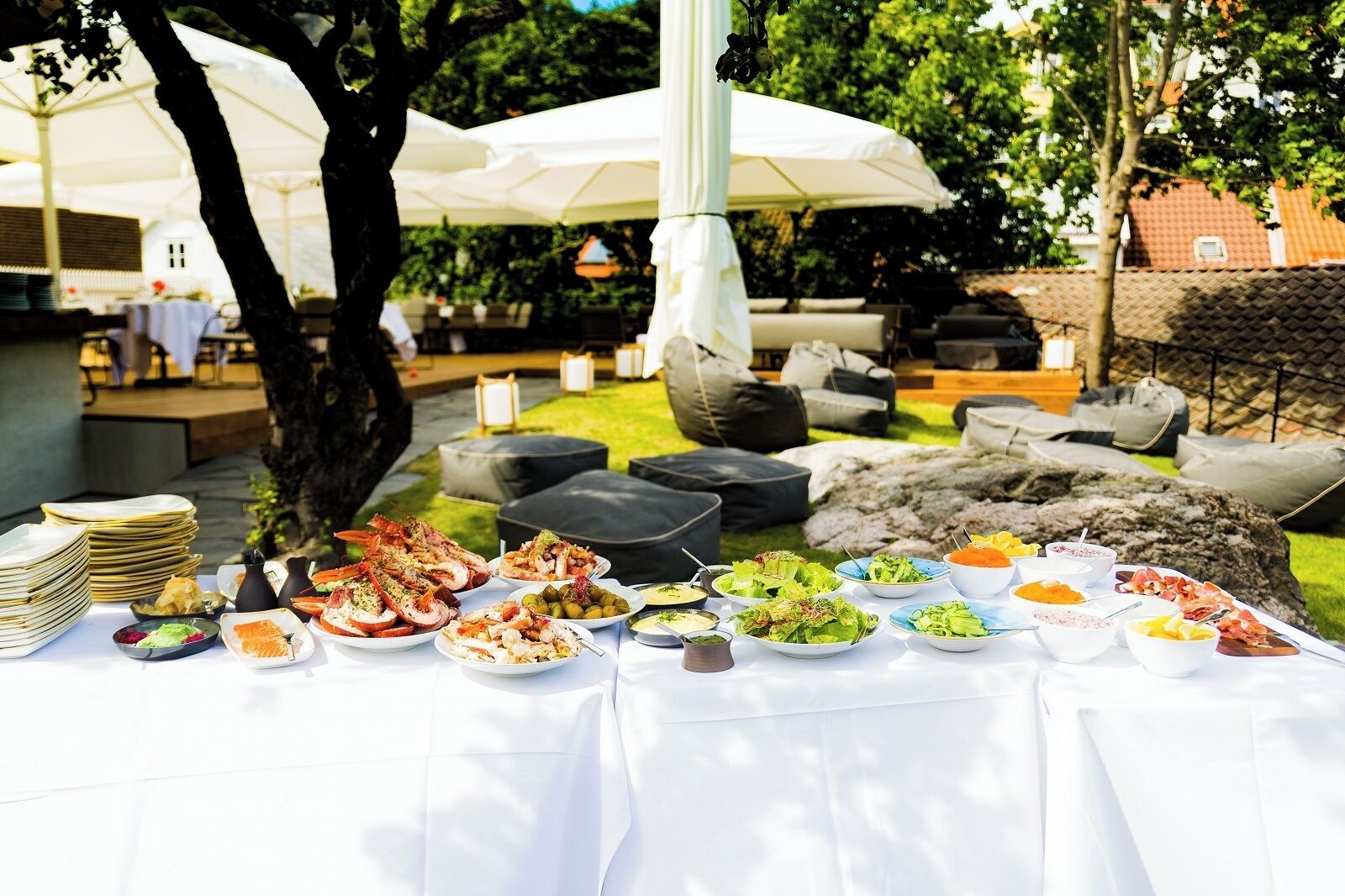 An outdoor dining area with a variety of dishes on a table, surrounded by outdoor seating and umbrellas.