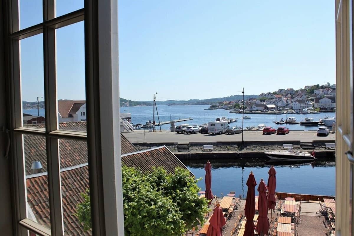 Blick vom Fenster auf einen Hafen mit Booten, einer Anlegestelle und einer Stadt in der Ferne.
