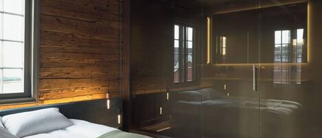 Un dormitorio moderno con pared de madera, cama grande y mampara de vidrio.