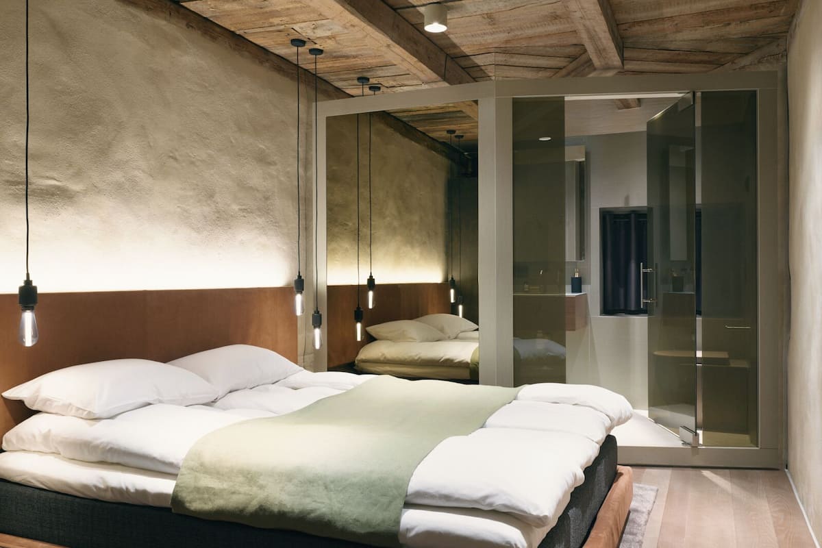Ein modernes Schlafzimmer mit Holzboden, einem Bett mit weißer Bettwäsche und einer Glastrennwand.