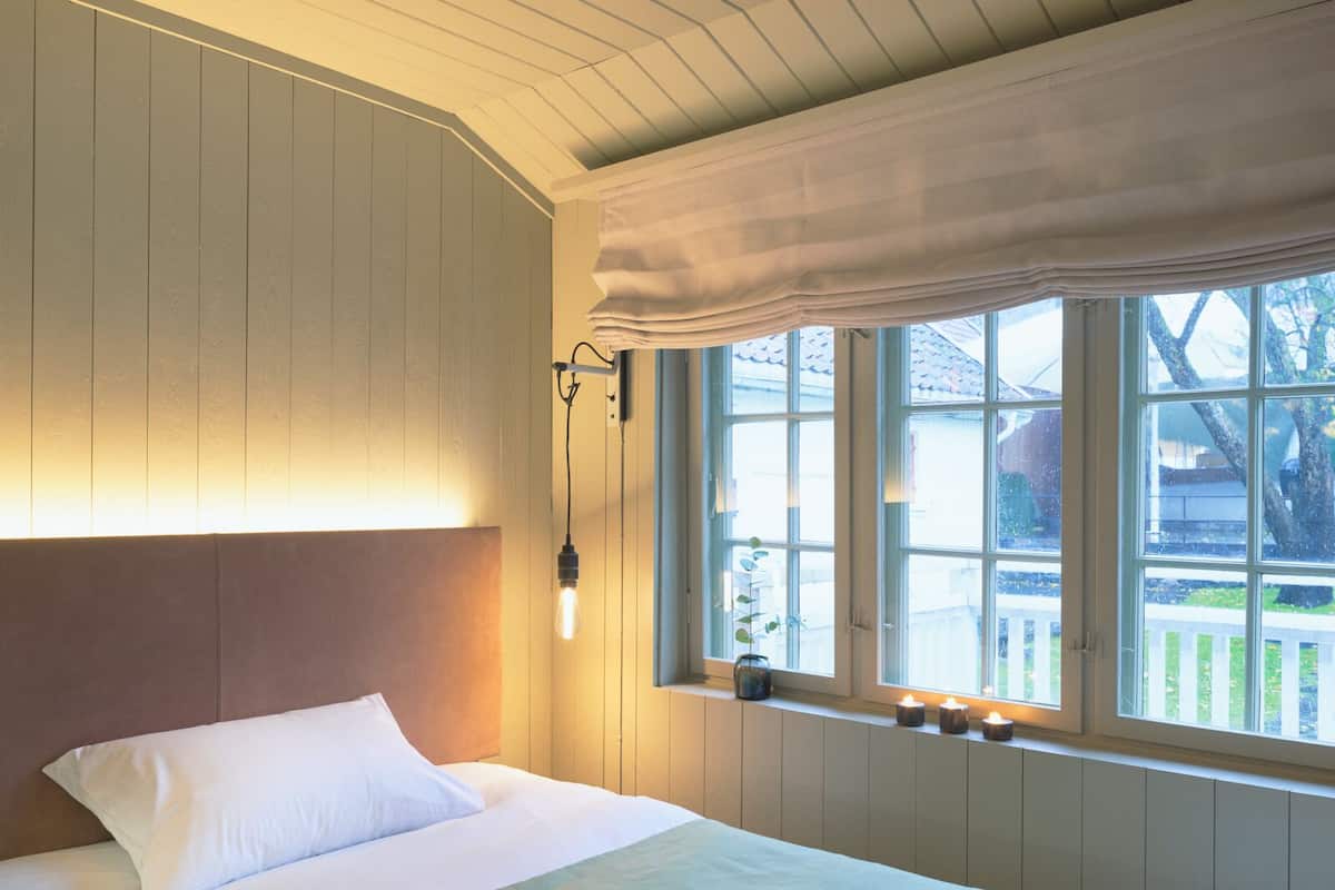 Ein Schlafzimmer mit einem großen Bett, einer Kopfteil, einem Fenster mit Vorhängen und einer Wandleuchte.