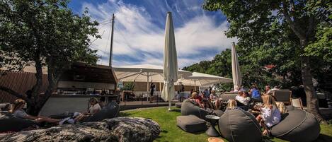 Espaço de estar ao ar livre com formações rochosas e poltronas de saco, cercado por árvores e guarda-sóis.